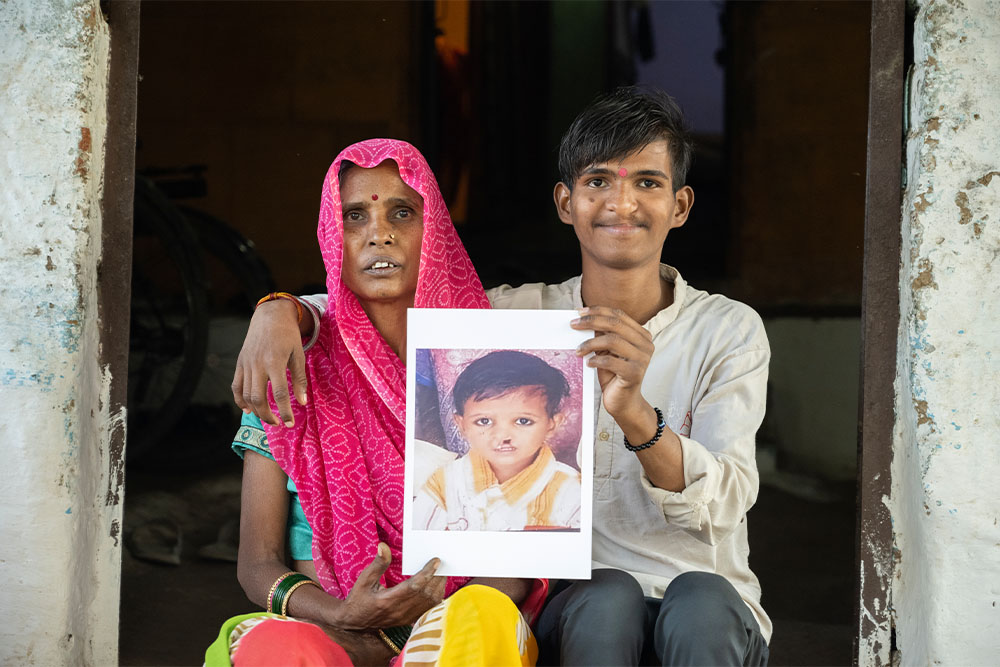 Sujal smiling with his mother, Malti and holding a picture of himself before cleft surgery