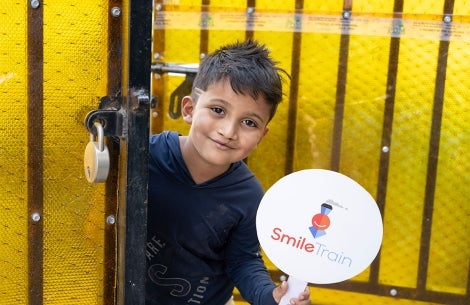 Abhay smiling and holding a Smile Train sign after cleft surgery
