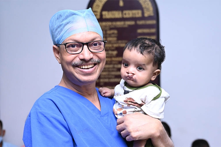 Dr Subodh smiling and holding a cleft-affected baby