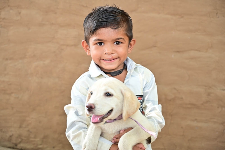 Jairaj smiling and holding a dog after cleft surgery