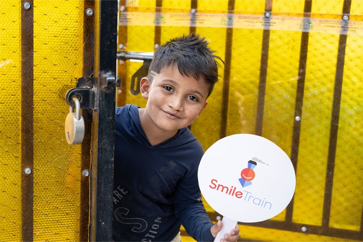 Abhay smiling and holding a Smile Train sign after cleft surgery