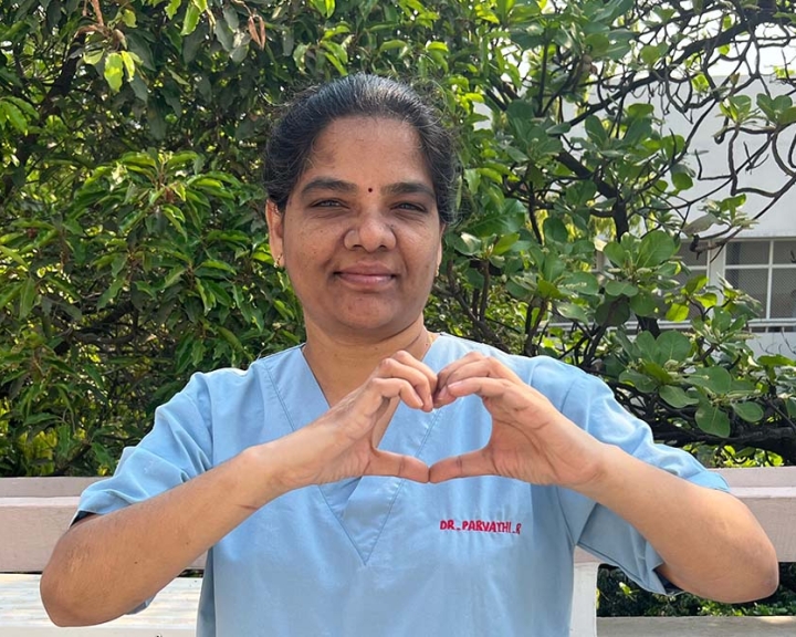 Dr R Parvathi smiling and holding up the International Women's Day heart sign