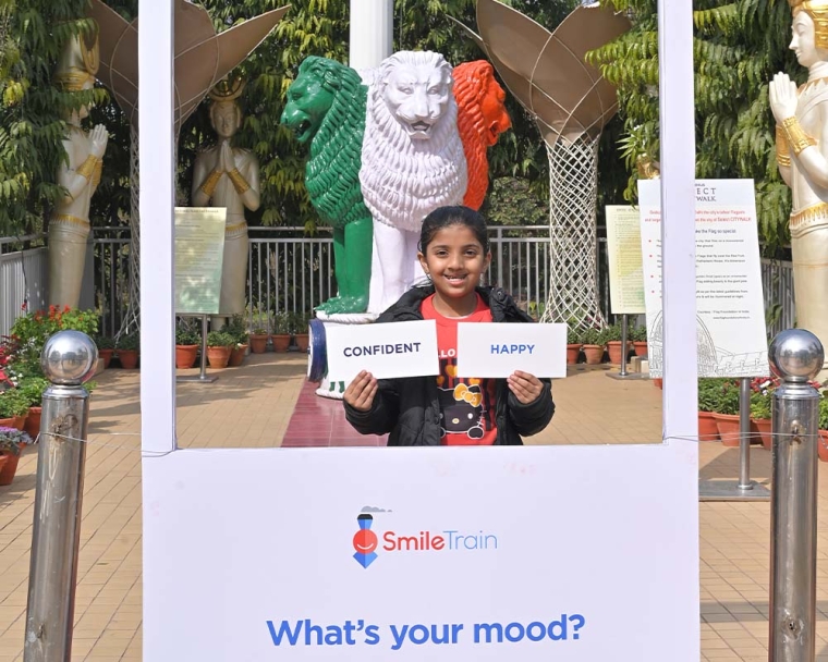 Smile Train patient holding signs saying "confident" and "happy" at a "What's your mood?" booth